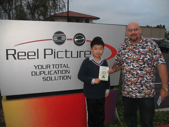 Perry Chen and Keith Wright in front of large sign with Reel Picture logo